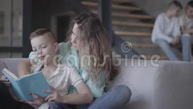 年轻漂亮的母亲和儿子坐在沙发上看书的画像，而她的两个孩子则坐在沙发上